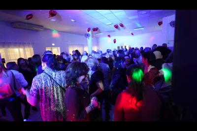 Salle de réception décorée pour un mariage, avec tables dressées, fleurs blanches et rouges, et arche florale en arrière…