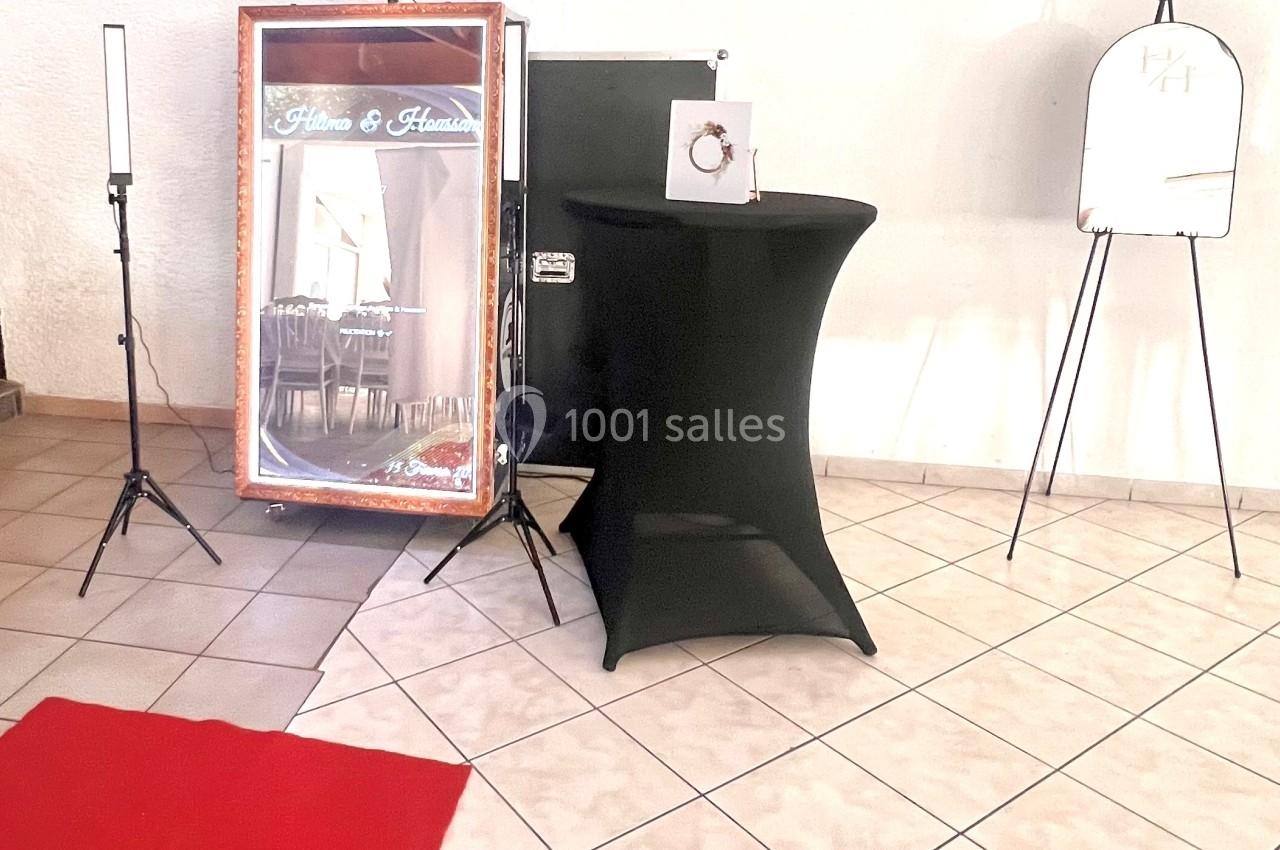 Miroir photobooth entouré d'équipements sur trépieds, avec une table noire et un chevalet dans une pièce carrelée.