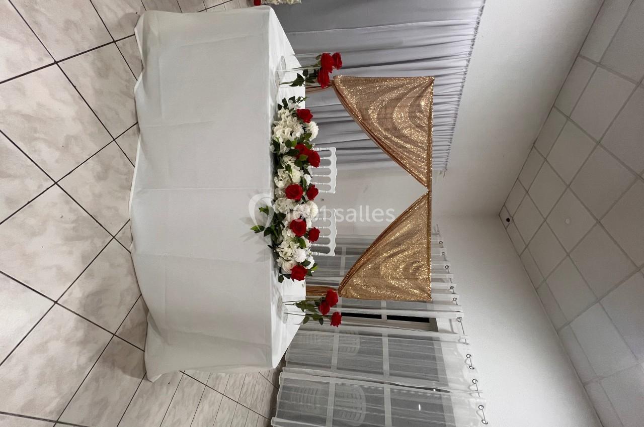 Table décorée avec des fleurs rouges et blanches, ornée d'un voile doré triangulaire, dans une salle carrelée.