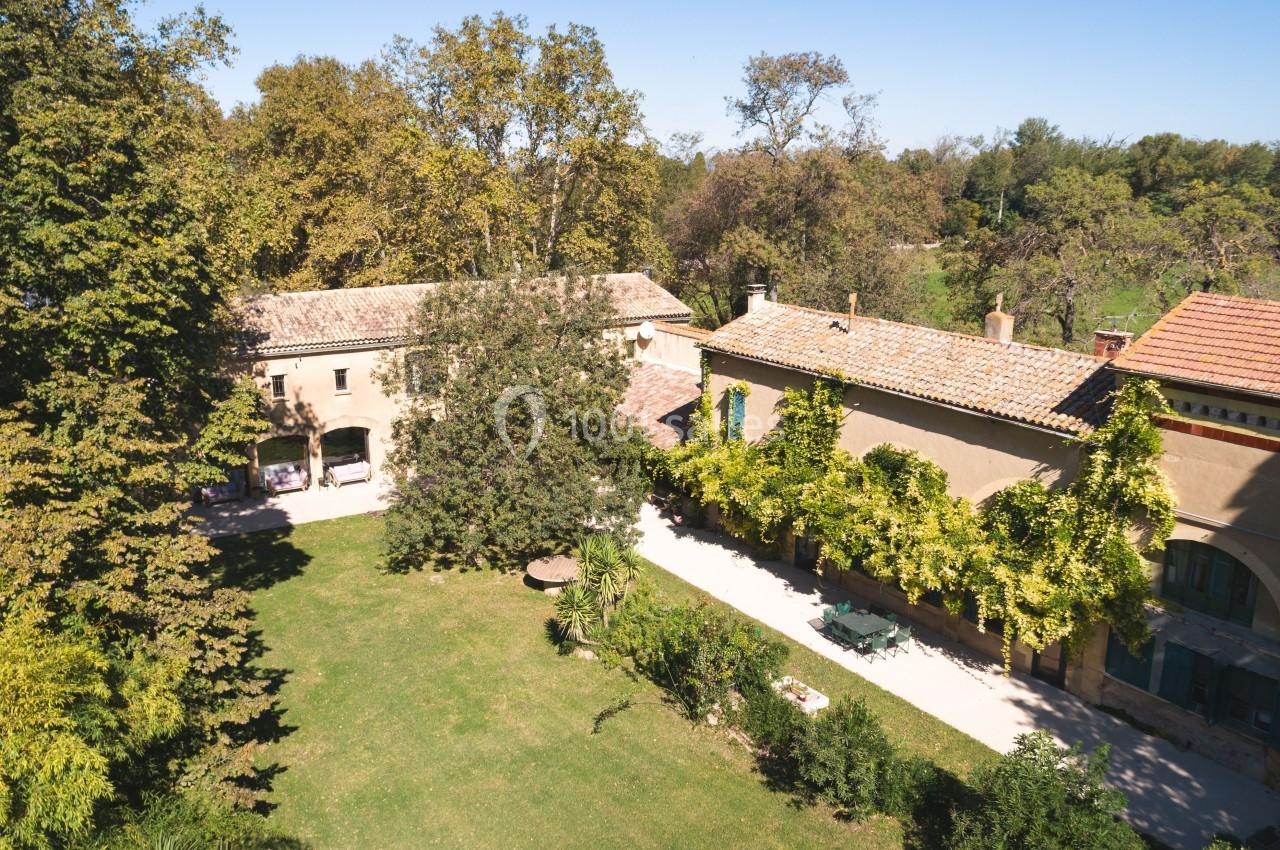 Vue aérienne d'une grande maison en pierre entourée d'arbres et d'un jardin verdoyant par une journée ensoleillée.