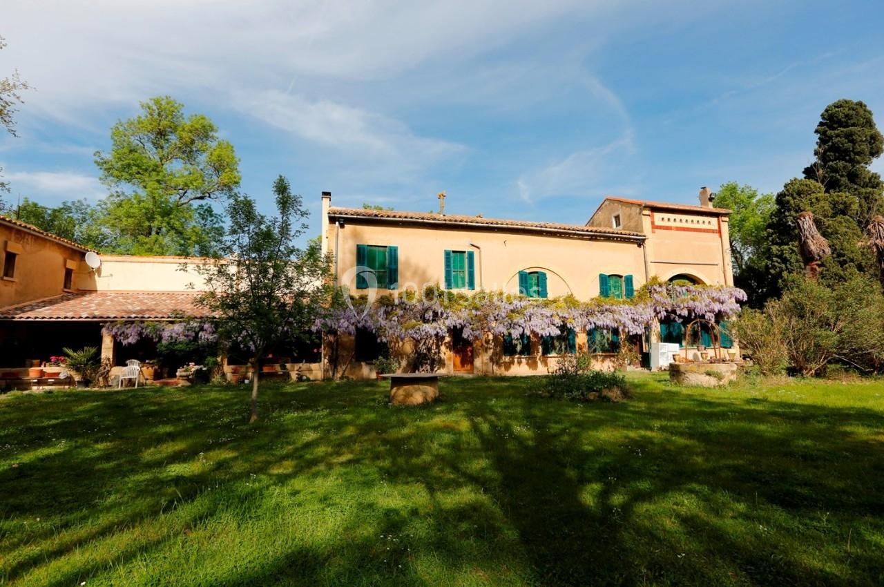 Façade d'une maison provençale entourée de verdure, ornée de glycines en fleurs sous un ciel dégagé.