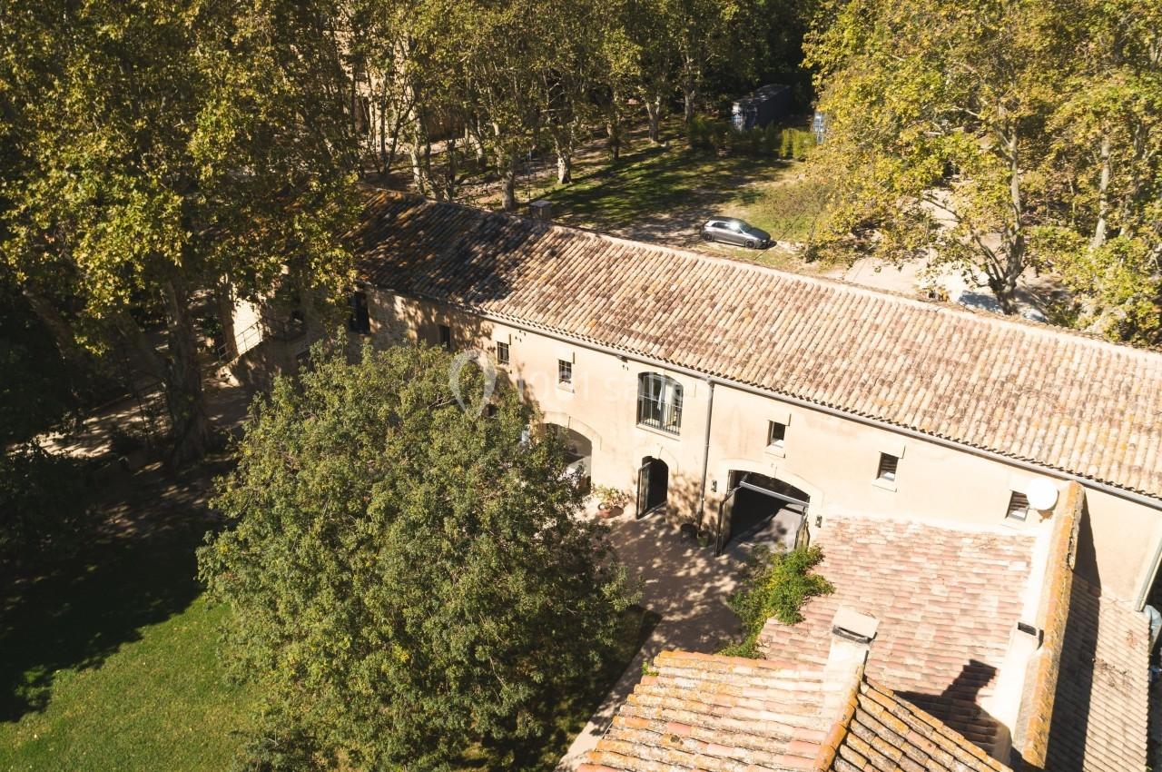 Vue aérienne d'un bâtiment ancien en pierre entouré d'arbres et d'une pelouse, avec une route à proximité.