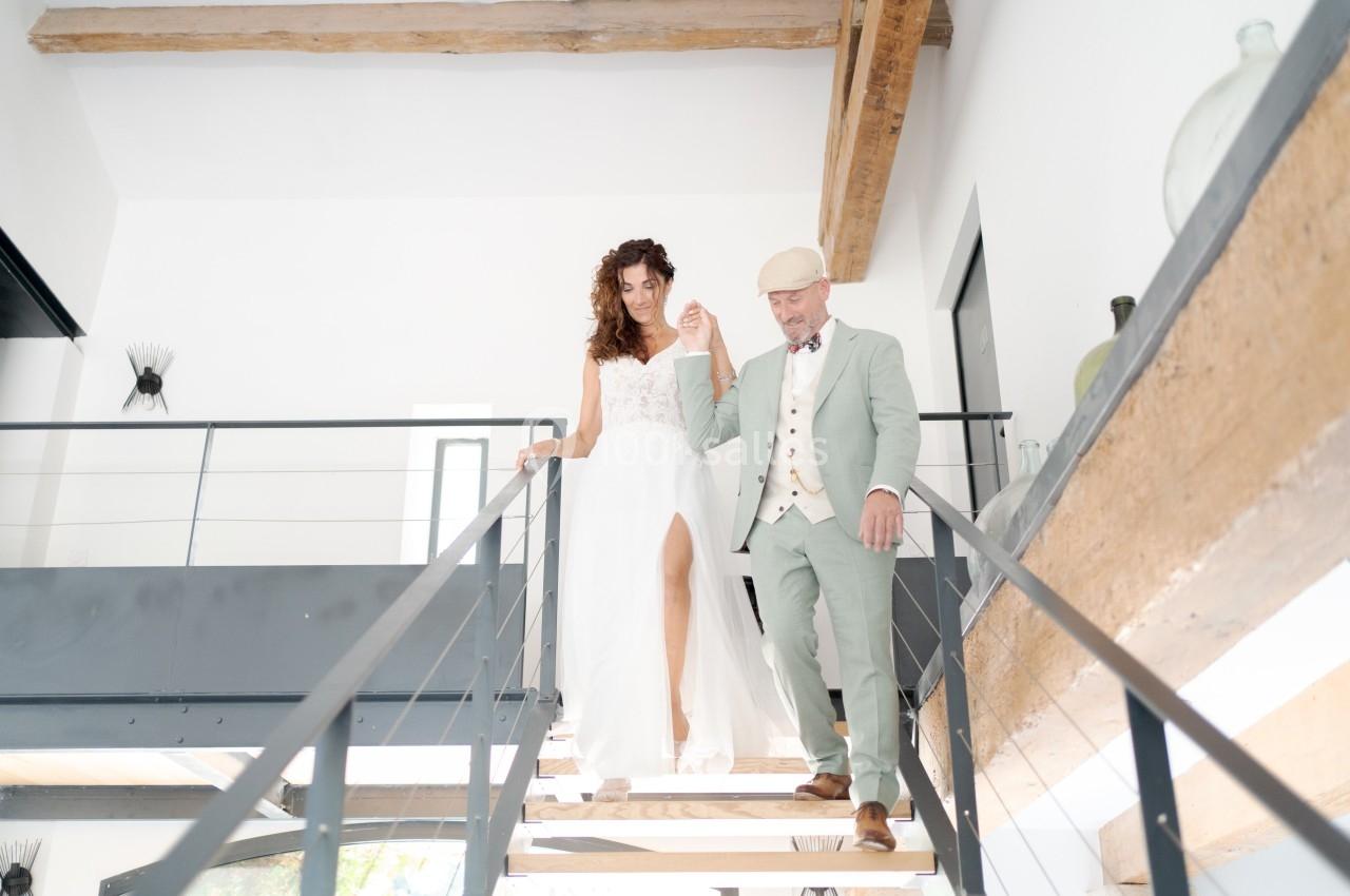 Un couple élégant descend un escalier moderne dans un intérieur lumineux avec poutres apparentes.