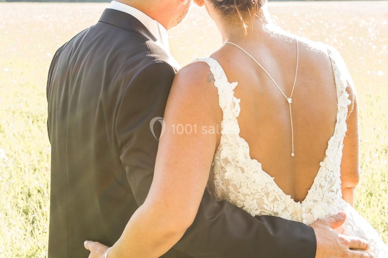 Un couple en tenue de mariage vu de dos, debout dans un champ ensoleillé.