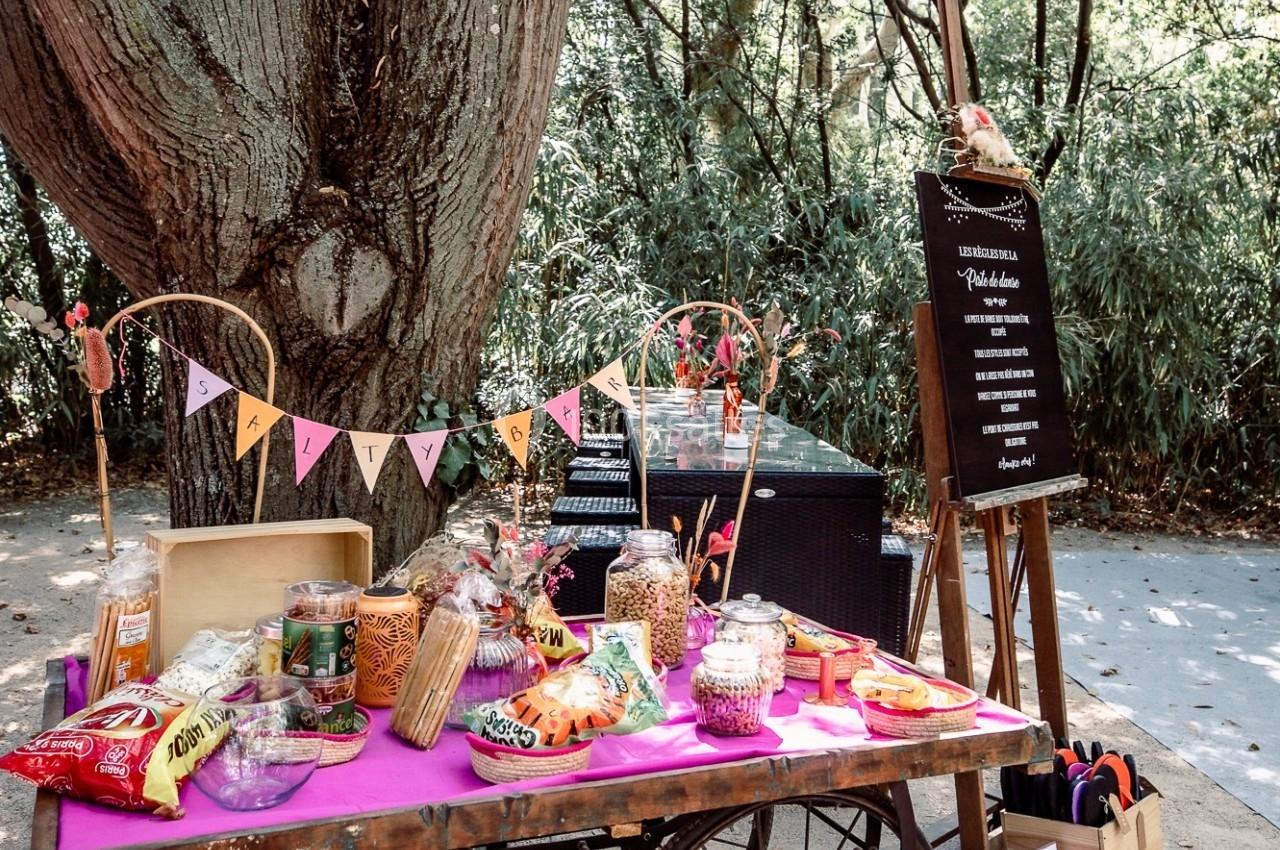 Chariot en bois décoré avec des guirlandes, rempli de snacks et bonbons, installé sous un grand arbre en extérieur.
