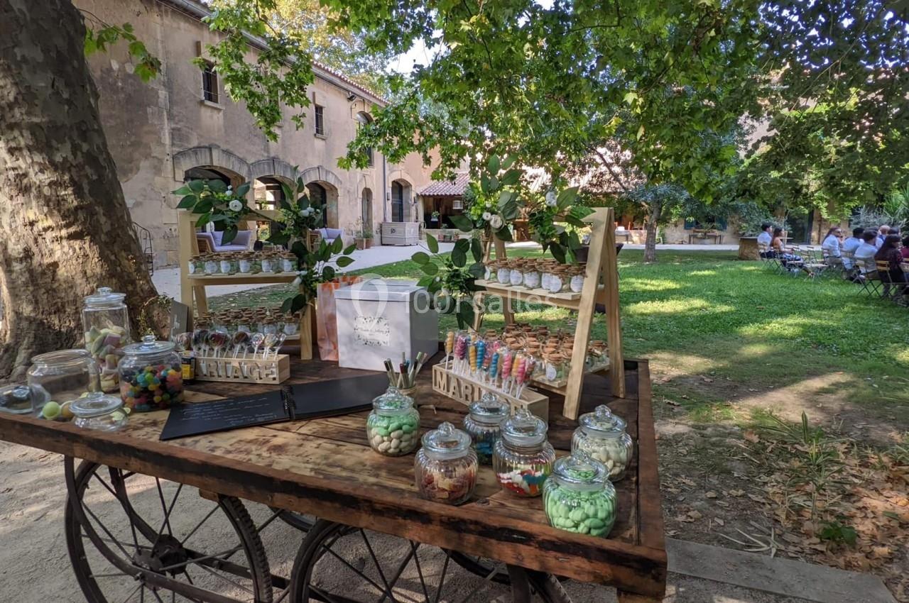 Table en bois avec des bonbonnières remplies de friandises, disposée dans un jardin près d'un bâtiment ancien.