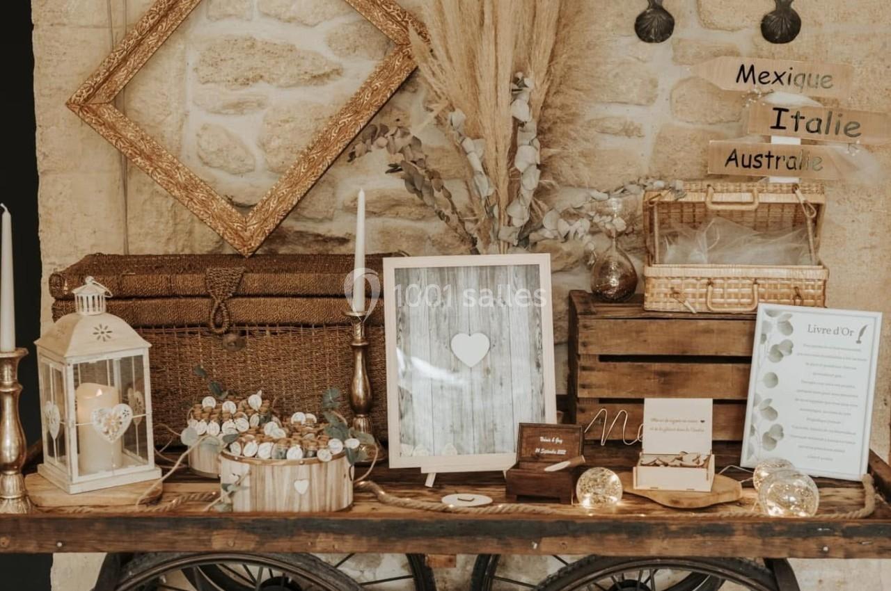 Table en bois sur roues décorée d'objets rustiques, cadres, bougies, fleurs séchées et accessoires vintage contre un mur en…