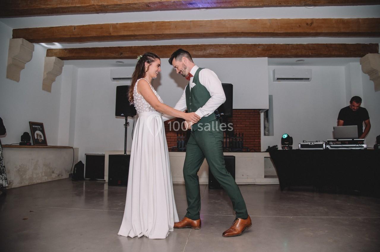 Un couple danse ensemble dans une salle avec un plafond en poutres apparentes et un DJ en arrière-plan.