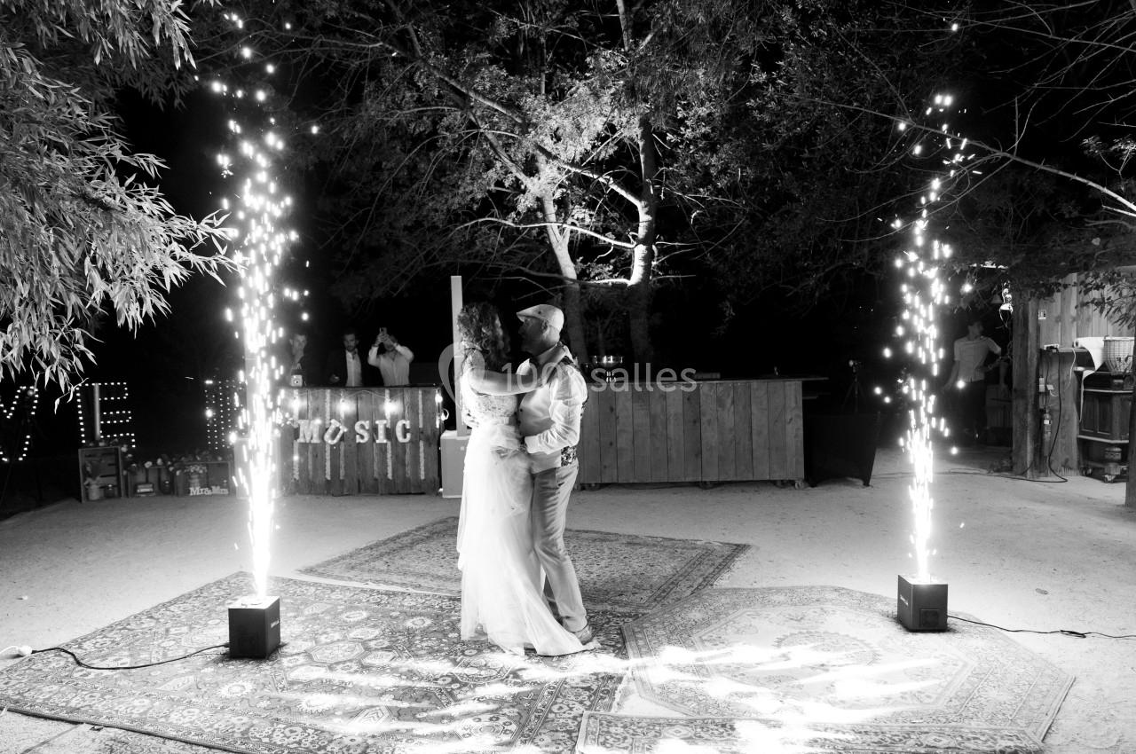 Un couple danse sous des étincelles lumineuses dans un décor extérieur nocturne avec tapis et arbres.