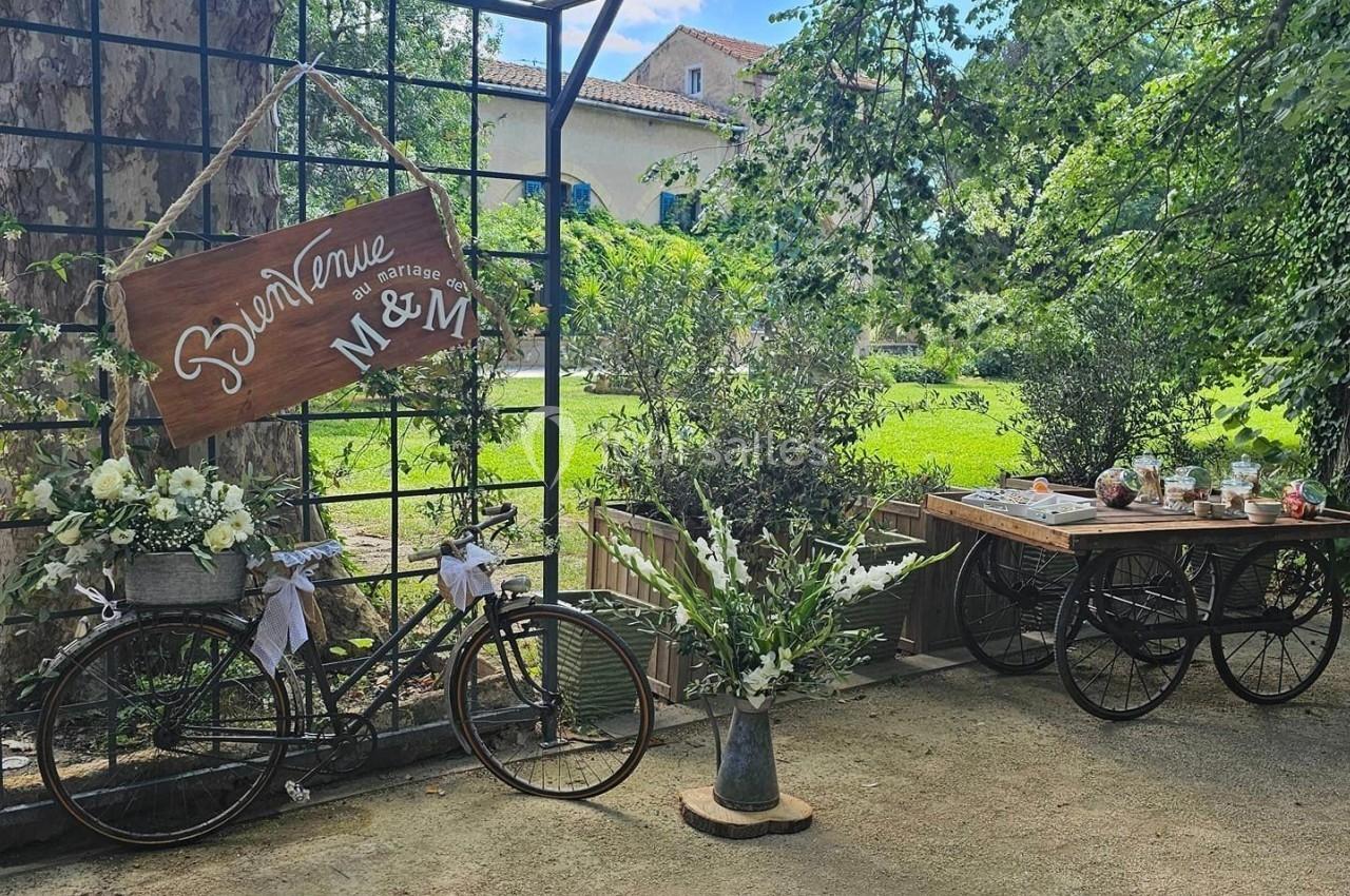 Deux vélos décorés de fleurs et un panneau en bois dans un jardin verdoyant, avec une table garnie d'objets.