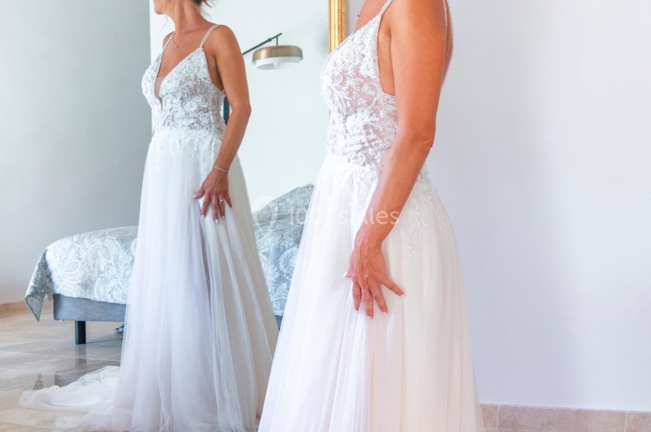 Femme en robe de mariée blanche se regardant dans un grand miroir doré, dans une pièce lumineuse.