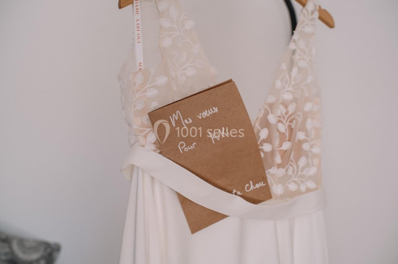 Robe de mariée blanche avec détails en dentelle, sur laquelle est posé un carnet marqué ’Mes vœux pour Kiki’.