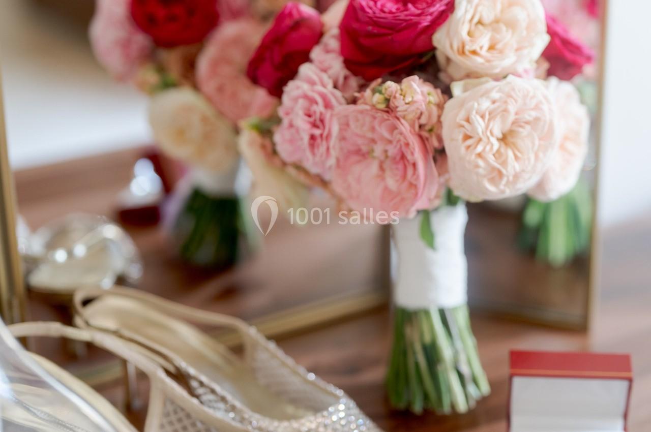 Bouquet de fleurs roses et rouges, escarpins perlés et boîte à alliances posés sur une table devant un miroir.