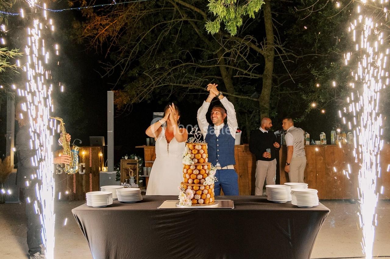 Un couple célèbre son mariage devant une pièce montée éclairée par des étincelles, en extérieur de nuit.