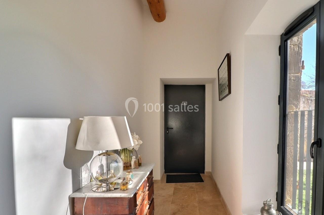 Couloir lumineux avec une commode en bois, une lampe, des décorations et une porte noire au fond.