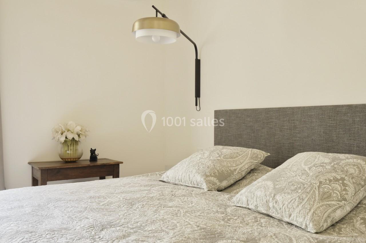 Lit double avec couvre-lit à motifs, deux coussins assortis, lampe murale et table de chevet avec vase de fleurs.