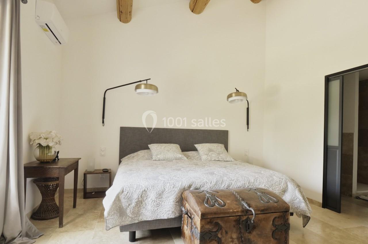 Chambre lumineuse avec lit double, poutres apparentes, table en bois, coffre ancien et appliques murales modernes.