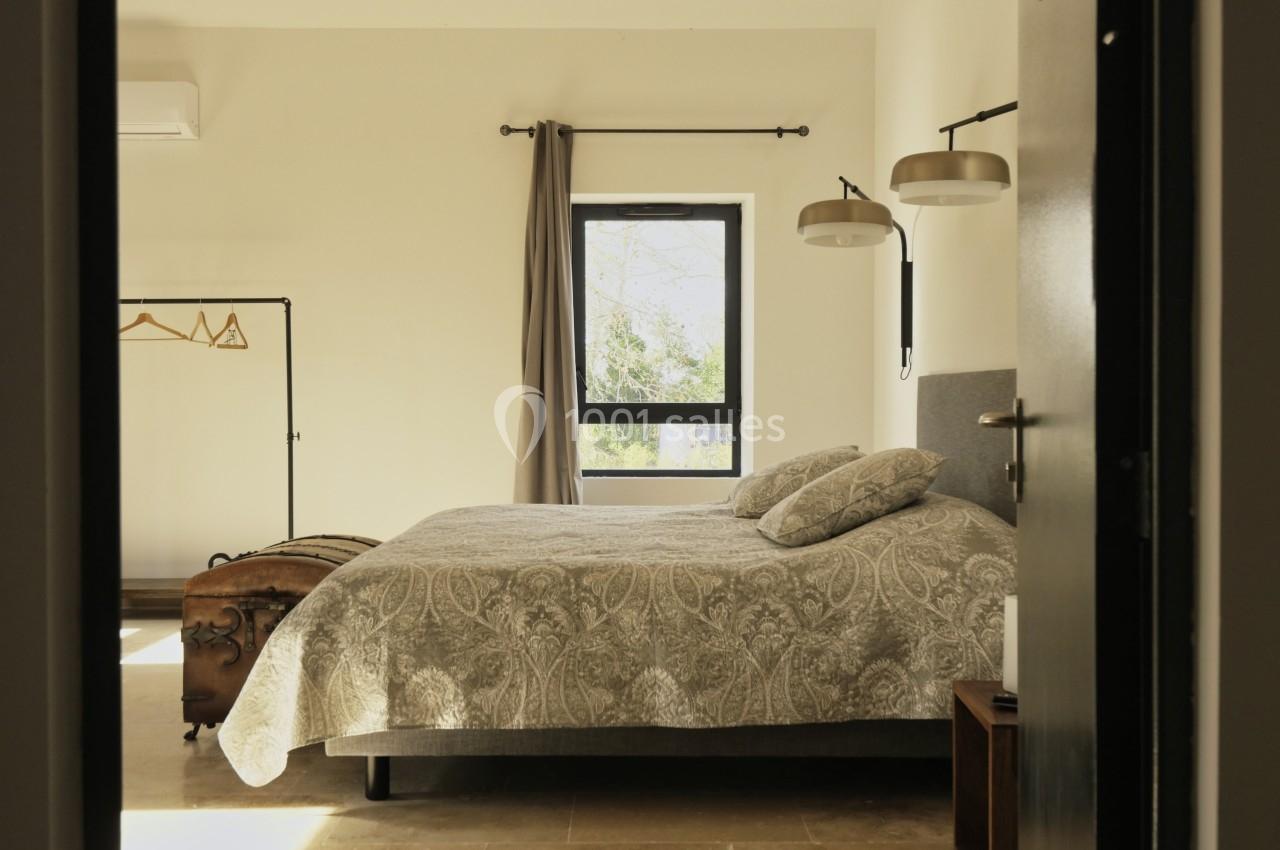 Chambre lumineuse avec un lit double, couvre-lit à motifs, fenêtre, portant à vêtements et appliques murales.