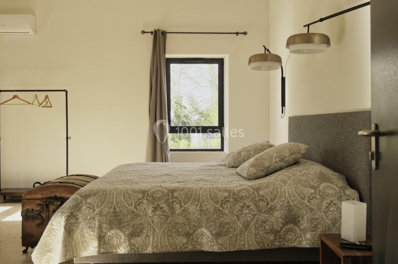 Chambre lumineuse avec un lit double, linge à motifs, fenêtre donnant sur l'extérieur et portant avec cintres.