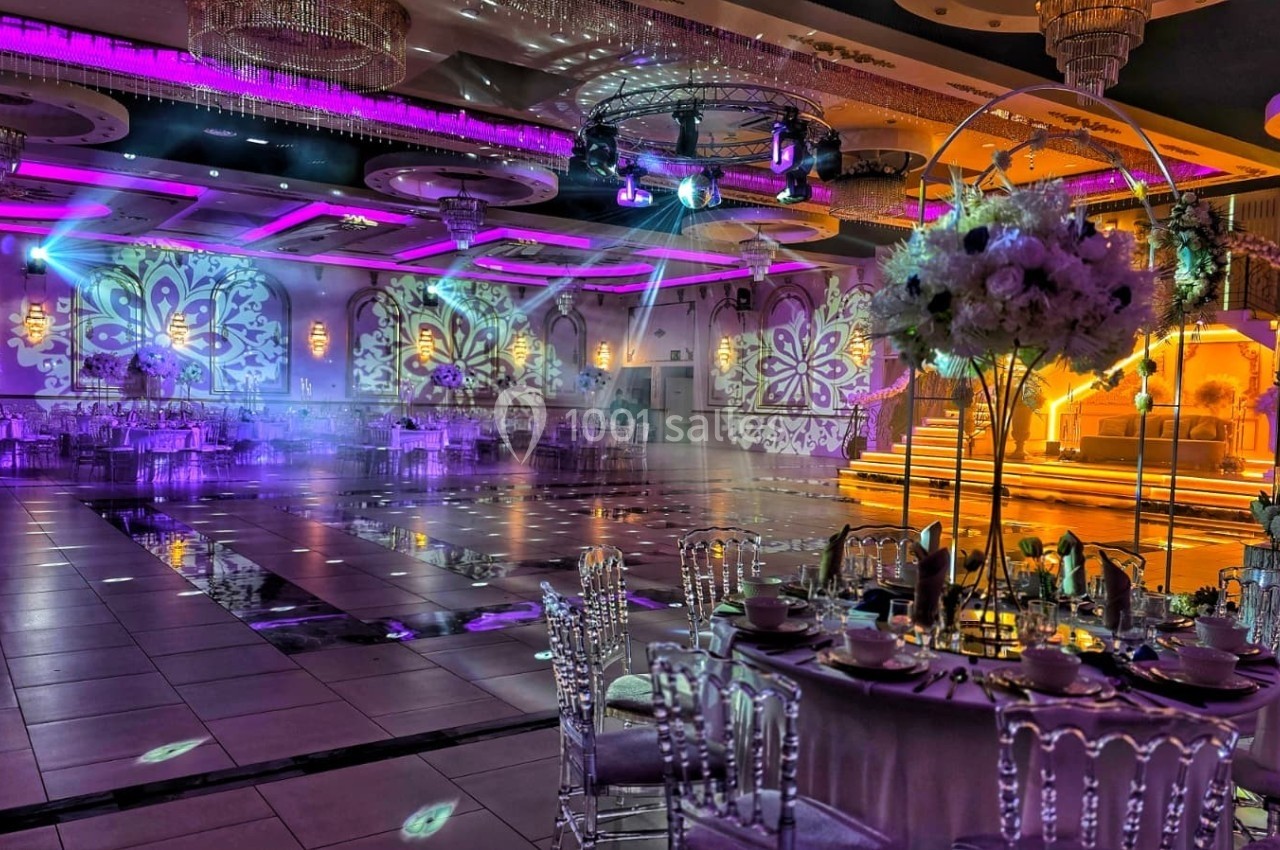 Salle de réception décorée avec des lumières colorées, des tables élégantes et une scène illuminée en arrière-plan.