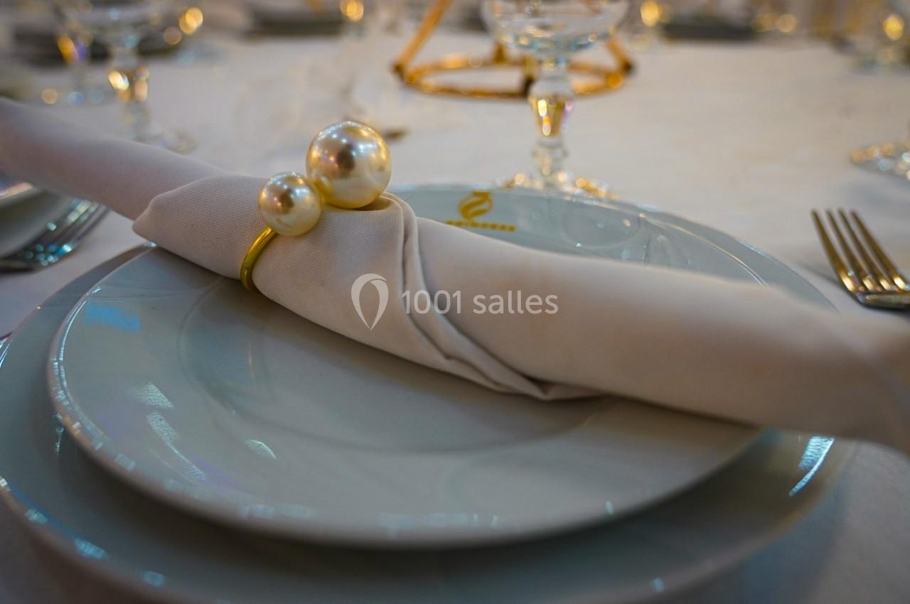 Serviette blanche roulée avec un anneau décoratif en perles, posée sur une assiette dans un décor de table élégant.