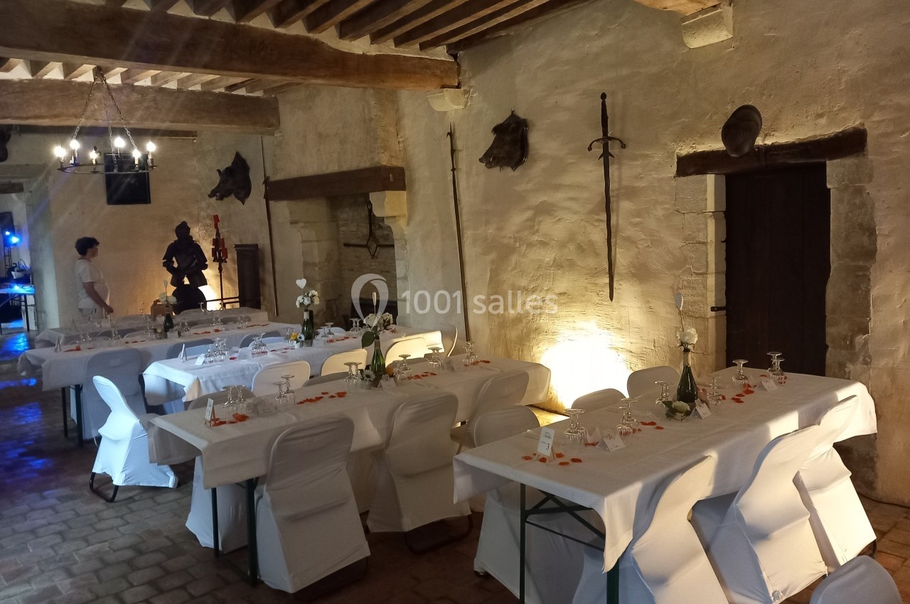 Salle de réception rustique avec tables dressées, murs en pierre, poutres apparentes et décoration médiévale.