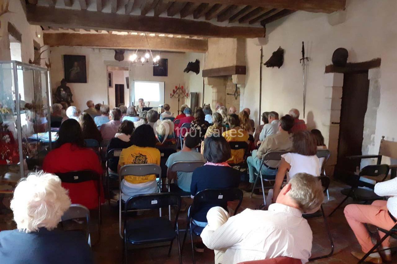 Un groupe de personnes assises dans une salle ancienne assistent à une présentation projetée sur un écran.