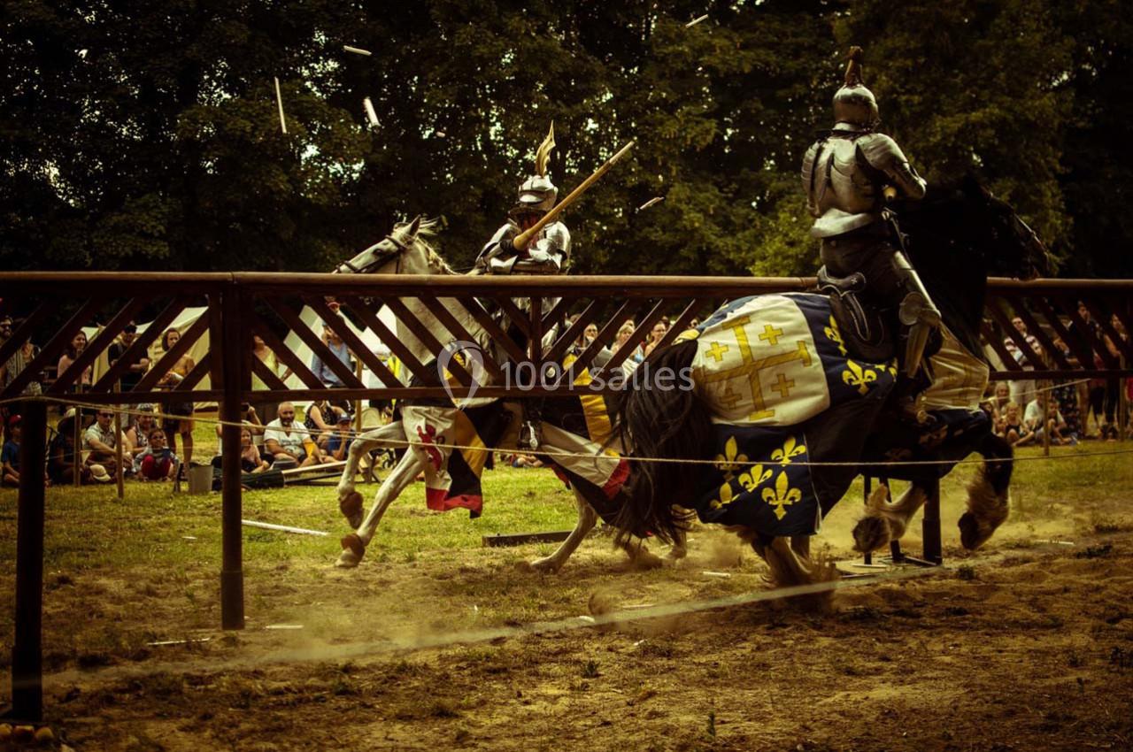 Deux chevaliers en armure s'affrontent à cheval lors d'un tournoi médiéval devant un public en plein air.