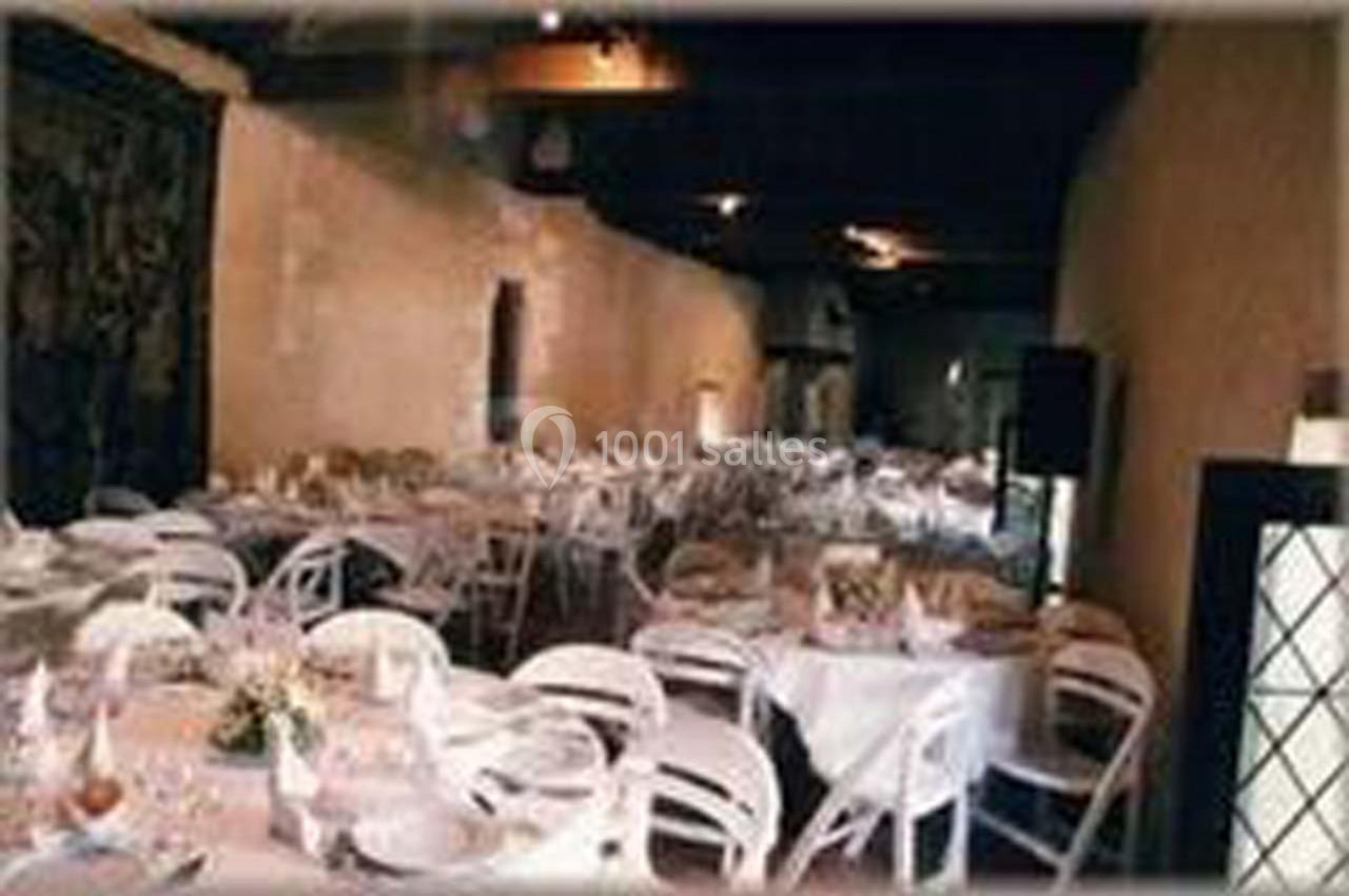 Salle de réception avec des tables rondes dressées et des chaises blanches, éclairée par une lumière tamisée.