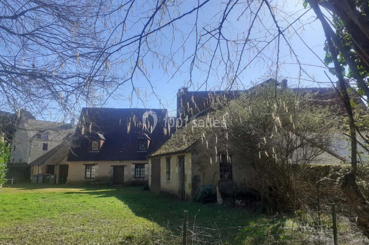 Maisons anciennes en pierre avec toits en pente, entourées d'arbres et d'un jardin ensoleillé.