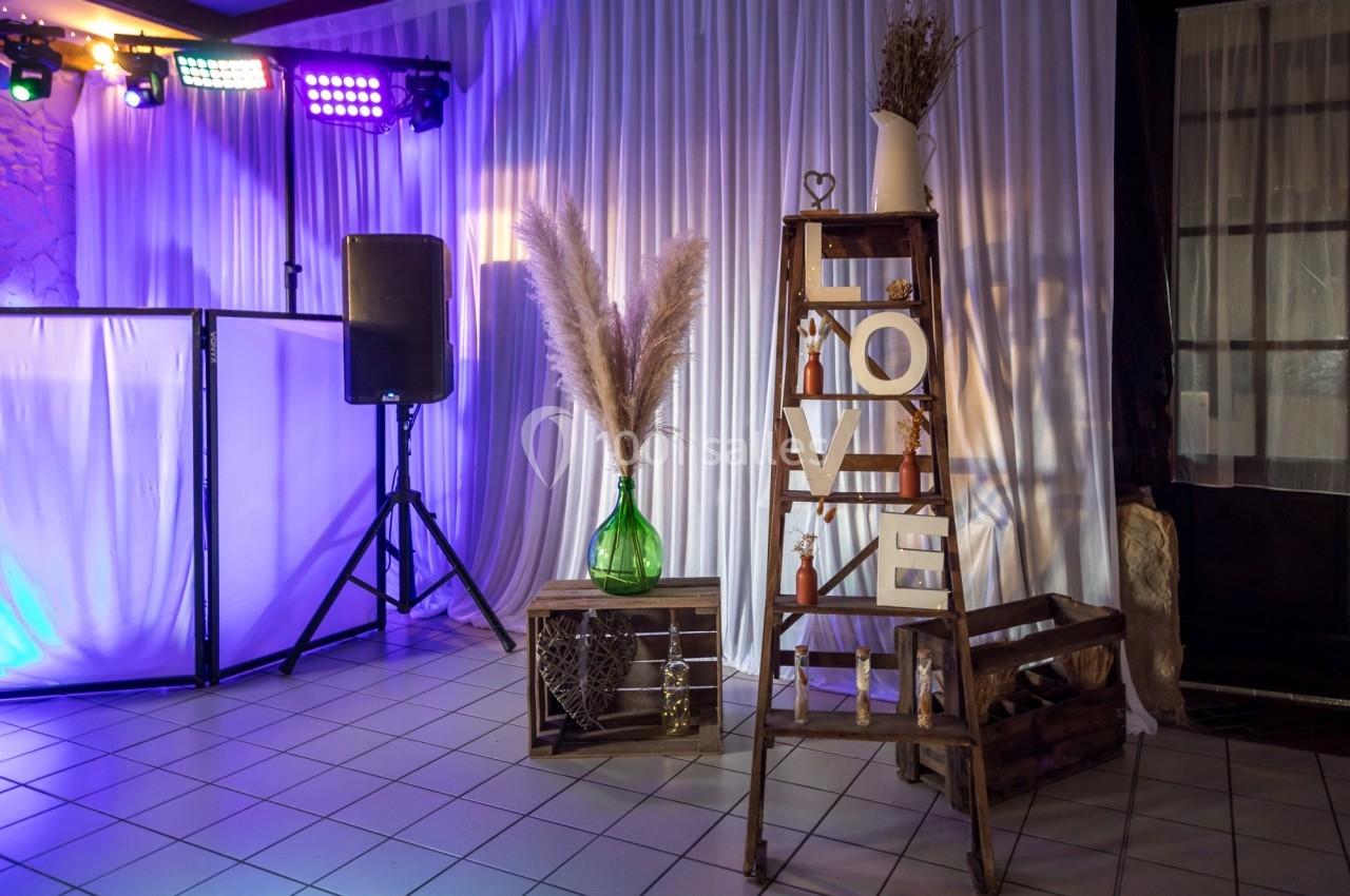 Location salle Beaubray (Eure) - Auberge de la Comtesse #13 Décoration de salle avec échelle en bois ornée de lettres ’LOVE’, pampas et vases, éclairage violet en arrière-plan.