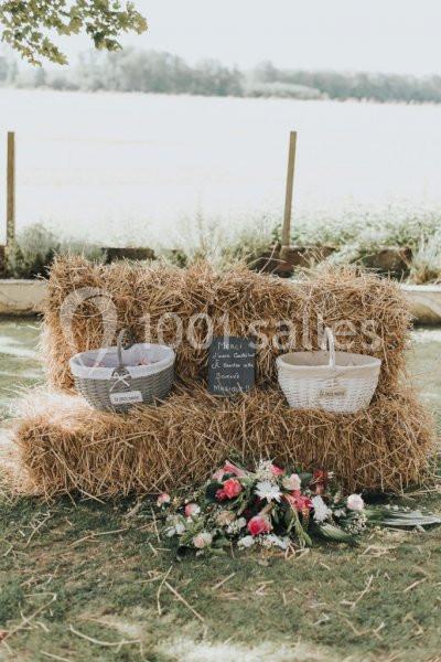 Mariage champêtre - Auberge de la comtesse Deux paniers posés sur des bottes de paille avec une ardoise et un bouquet de fleurs au sol, en extérieur.