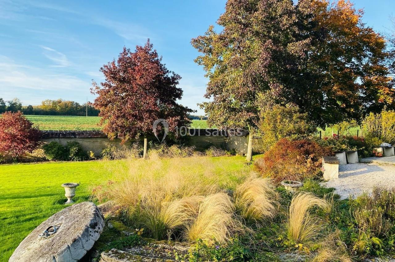 Mariage d'Automne - Auberge de la comtesse Jardin avec herbes hautes, arbres aux feuilles d'automne et vue sur un champ sous un ciel dégagé.