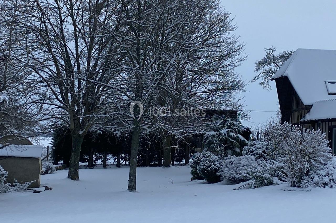 Mariage d'hiver - Auberge de la comtesse Paysage hivernal avec arbres dénudés et toits enneigés dans un jardin recouvert de neige.