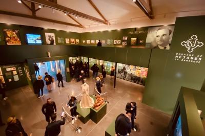 Grande salle vide avec un sol en pierre, plafond en bois avec poutres apparentes et lustres suspendus, décorée de plantes.