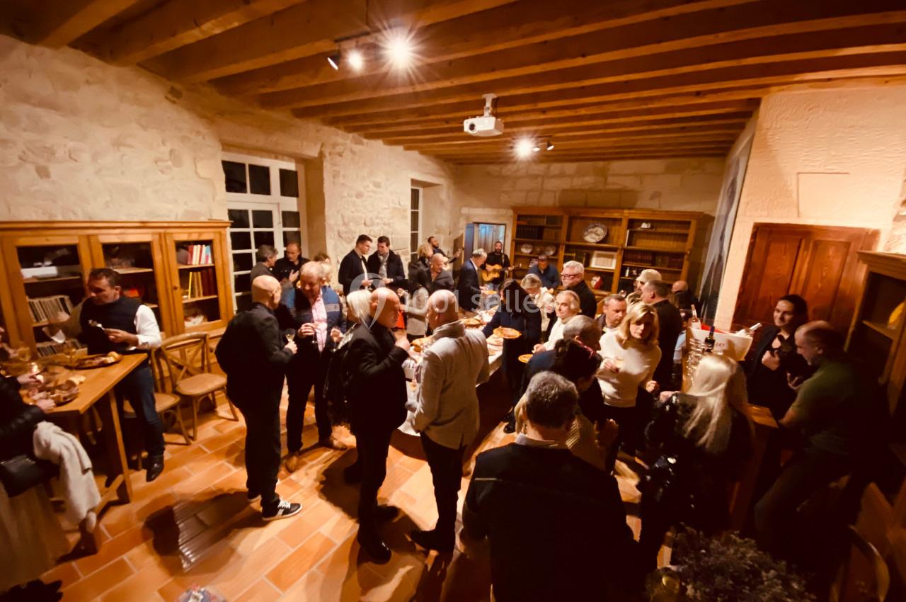 Groupe de personnes réunies dans une salle en bois et pierre, discutant et partageant un moment convivial.