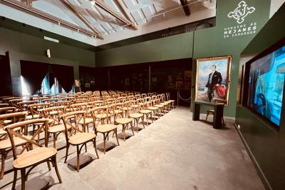 Grande salle vide avec un sol en pierre, plafond en bois avec poutres apparentes et lustres suspendus, décorée de plantes.