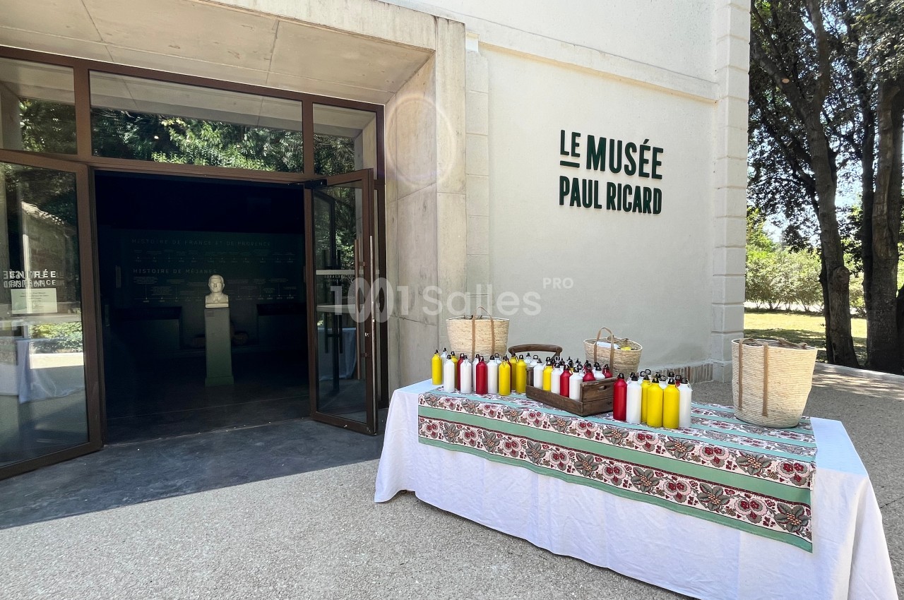 Entrée du musée Paul Ricard avec une table décorée présentant des bouteilles colorées et des paniers en osier.