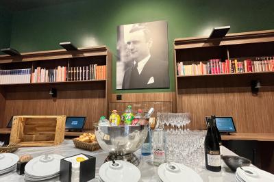 Grande salle vide avec un sol en pierre, plafond en bois avec poutres apparentes et lustres suspendus, décorée de plantes.