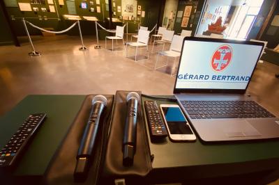 Grande salle vide avec un sol en pierre, plafond en bois avec poutres apparentes et lustres suspendus, décorée de plantes.