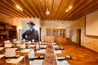 Grande salle vide avec un sol en pierre, plafond en bois avec poutres apparentes et lustres suspendus, décorée de plantes.