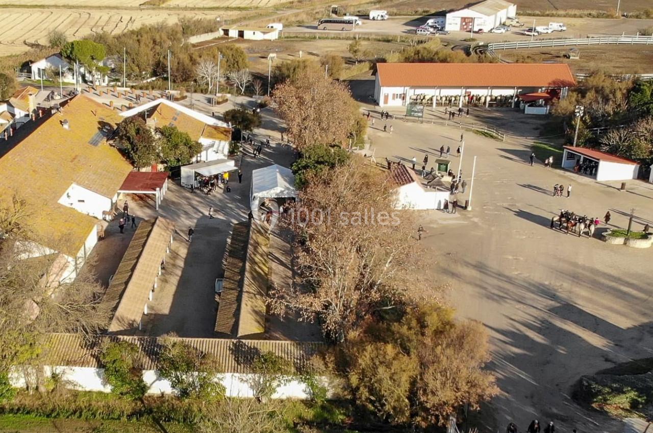 Vue aérienne d'un domaine rural avec bâtiments traditionnels, espaces ouverts et quelques arbres en automne.