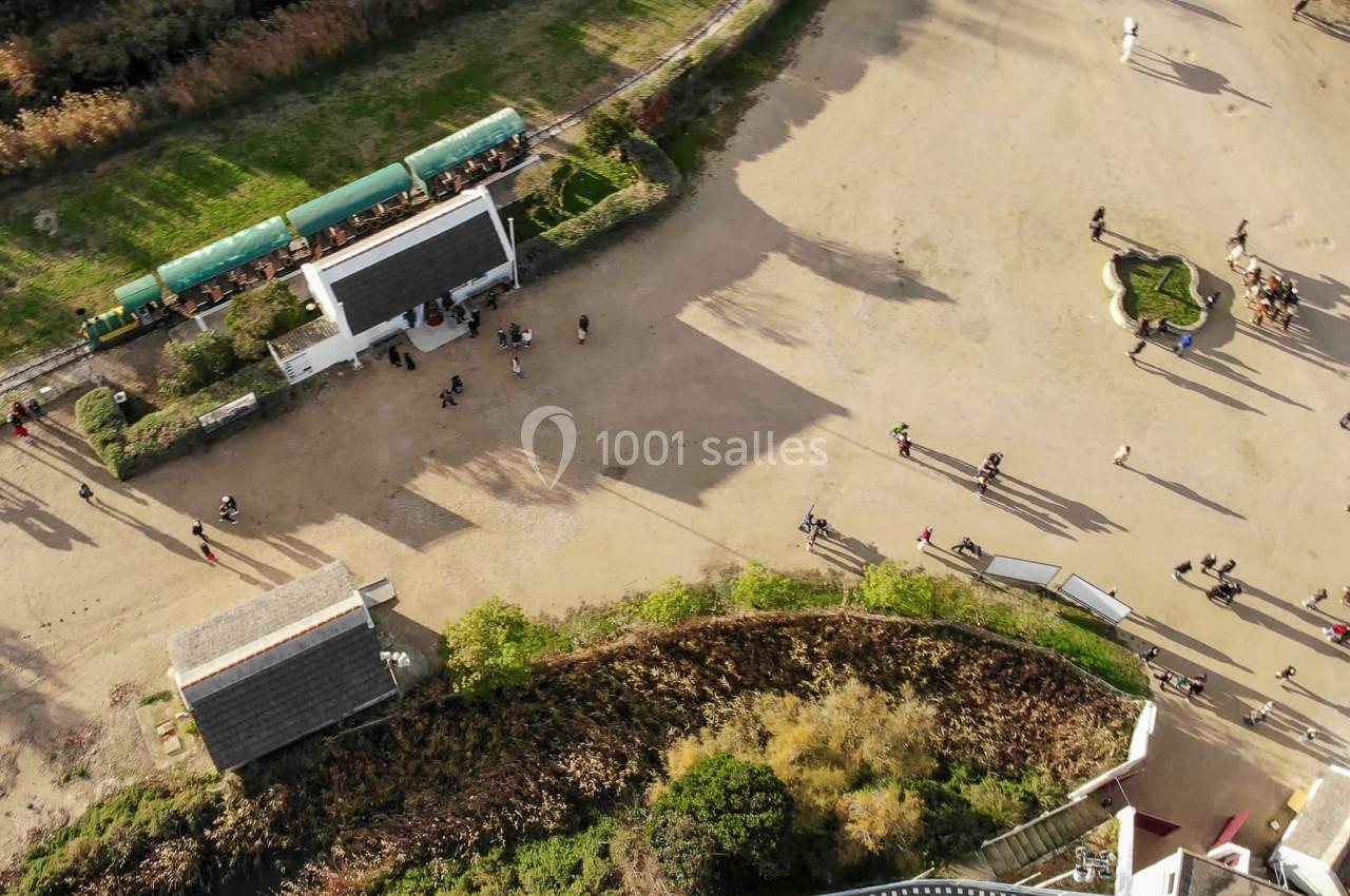 Vue aérienne d'une entrée de parc avec des visiteurs, un petit train vert et des espaces verts environnants.