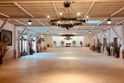 Grande salle vide avec un sol en pierre, plafond en bois avec poutres apparentes et lustres suspendus, décorée de plantes.