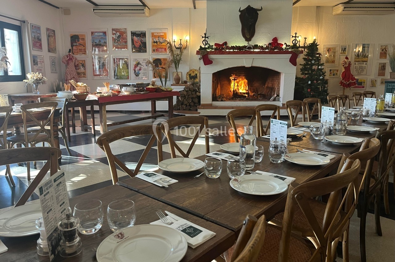 Salle de restaurant chaleureuse avec tables dressées, cheminée allumée et décorations de Noël.