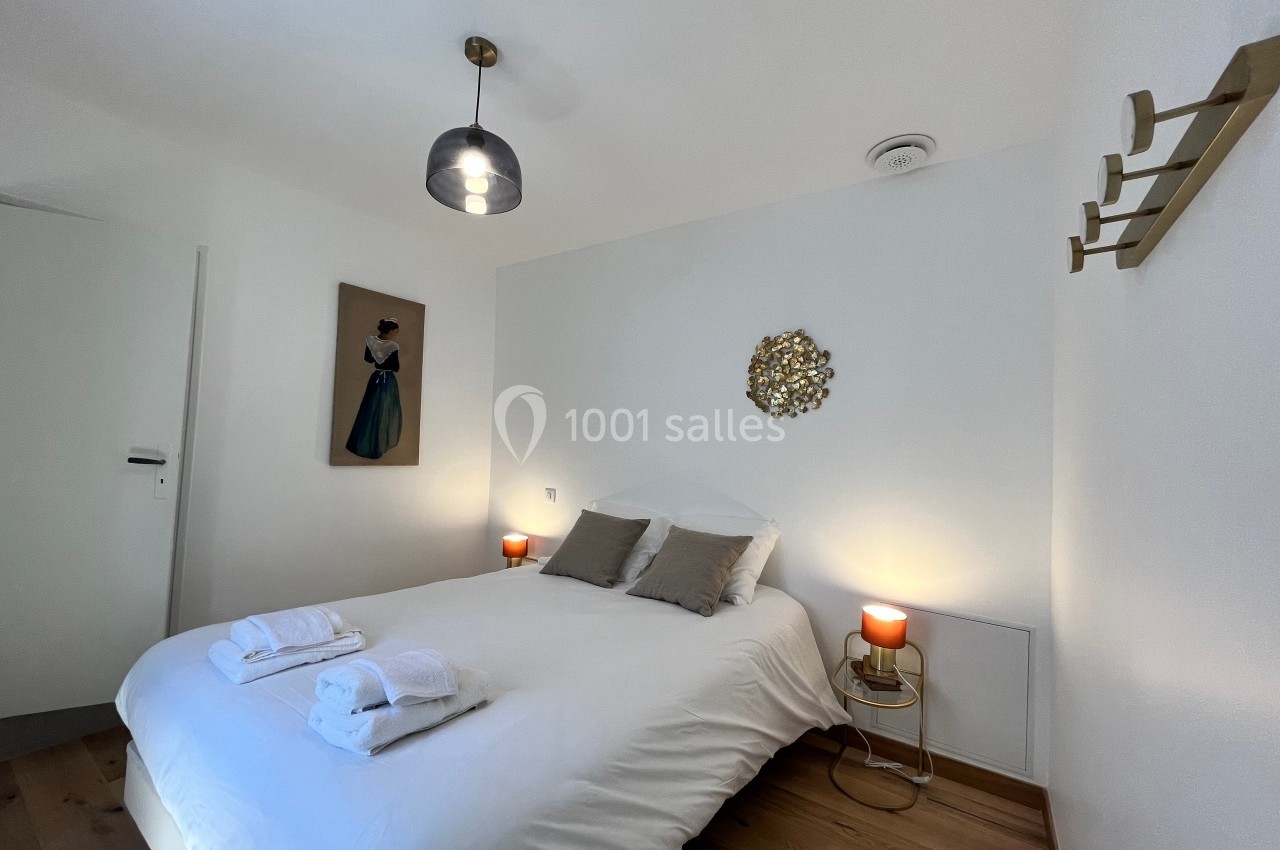 Chambre lumineuse avec lit double, décor sobre, deux lampes de chevet et des serviettes pliées sur le lit.