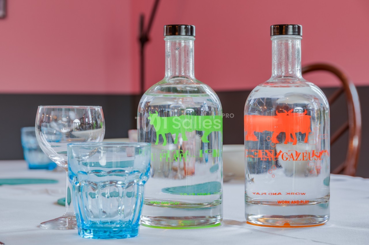 Deux bouteilles d'eau, une plate et une gazeuse, posées sur une table avec des verres transparents et bleus.