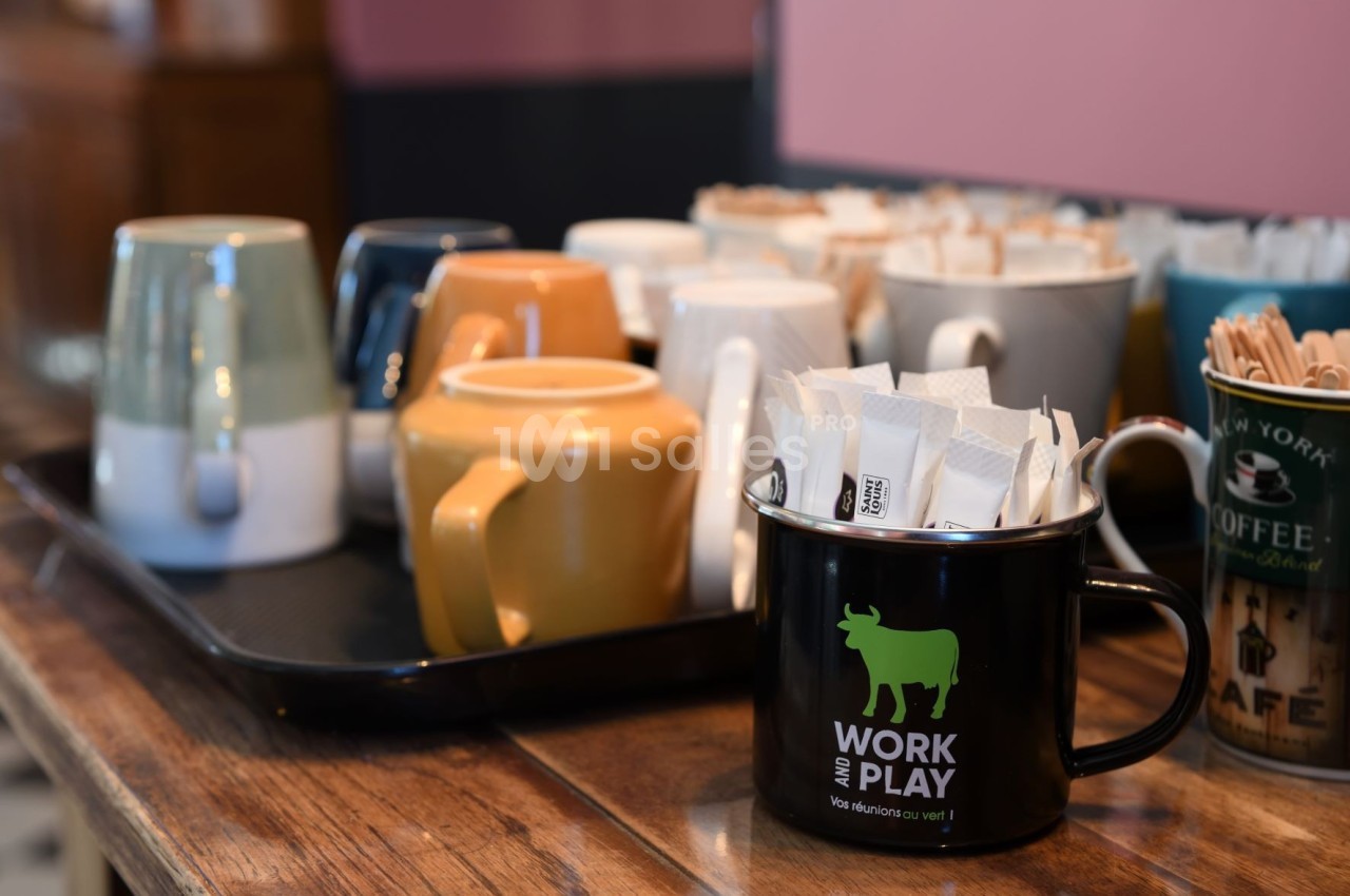 Tasses variées sur un plateau et une tasse noire contenant des sachets de sucre, posées sur une table en bois.