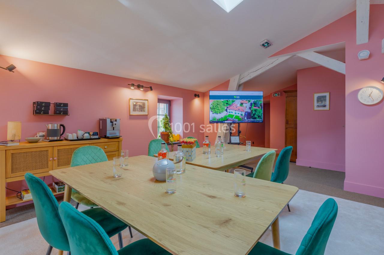 Salle de réunion lumineuse avec murs roses, tables en bois, chaises vertes et écran affichant une présentation.