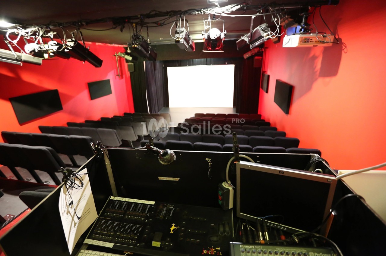 Salle de projection avec rangées de sièges noirs, écran blanc et cabine technique équipée à l'avant-plan.